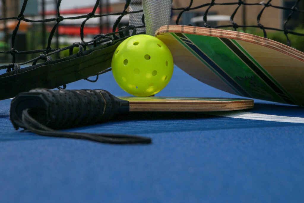 Close up of two pickleball paddles and whiffle balls under a net on a tennis pickleball court.