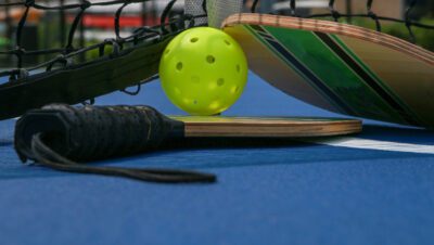 Close up of two pickleball paddles and whiffle balls under a net on a tennis pickleball court.